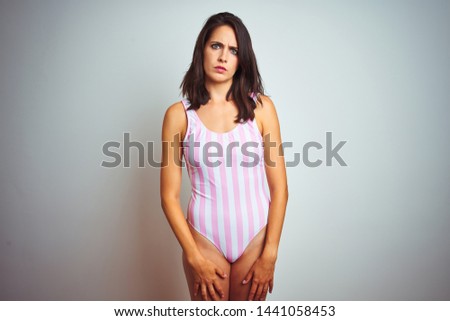 Young beautiful woman wearing striped pink swimsuit swimwear over isolated background skeptic and nervous, frowning upset because of problem. Negative person.