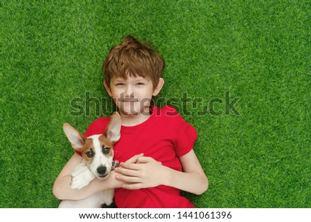 Child embracing puppy jack russell and lying on green carpet. High top view.