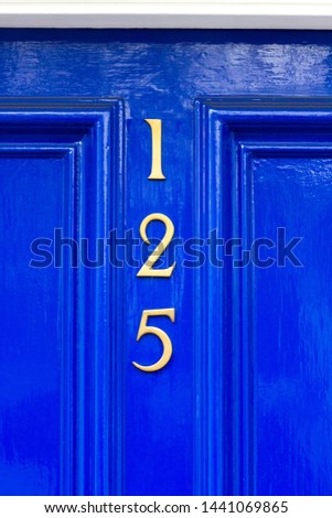 House number 125 with the one hundred twenty five in gold metal digits on a bright blue wooden front door and white door frame