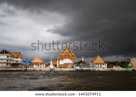 Beautiful Buddhist temple church at riverside under black clouds before heavy rain fall.