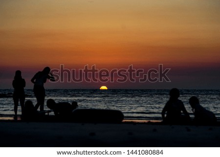 Silhouette group of people relaxing on beach at summer dark sunset.