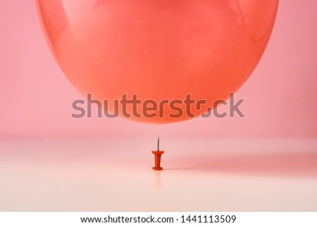  Red balloon fall on pin needle on pink background. Danger or protection concept