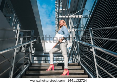 Blonde successful business woman standing on the stairs holding laptop. Walk into future. Confident woman concept. 