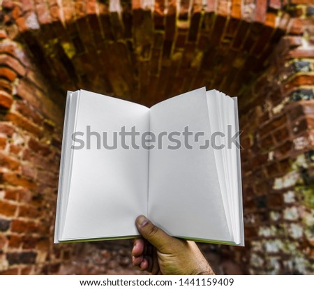 male hand hold Open white book is on red brick wall. abandoned brick wall background. empty blank - copy space for inscription. 