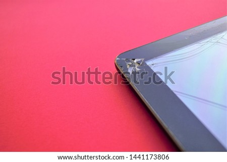 Angle of broken tablet with damaged screen with cracks on bright red background with space for text