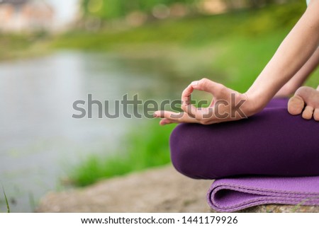 Yoga woman practicing yoga lesson, breathing, meditation, doing exercise Ardha Padmasana, half lotus pose with mudra gesture, closeup in summer on nature against the background of water.