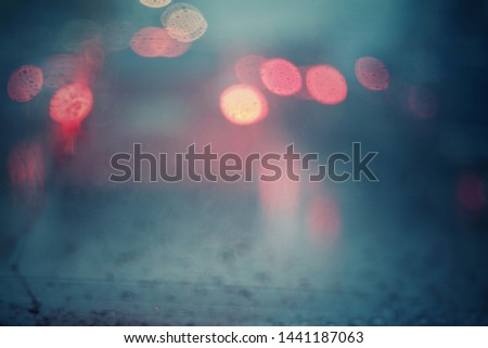 Abstract glittering bokeh lights of cars on traffic jam in city in rainy day with defocused droplets on glass of vehicle in foreground.