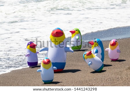 Beach toy background. Selective focus on a group of seven colorful inflatable rubber penguin toys at a sandy sunny beach. Space for advertising. Macro.