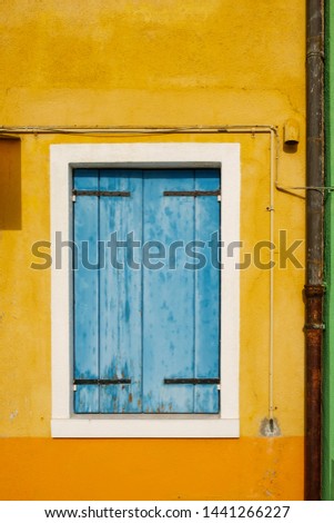 Old window with blue wooden closed blinds on the shabby yellow and orange wall facade
