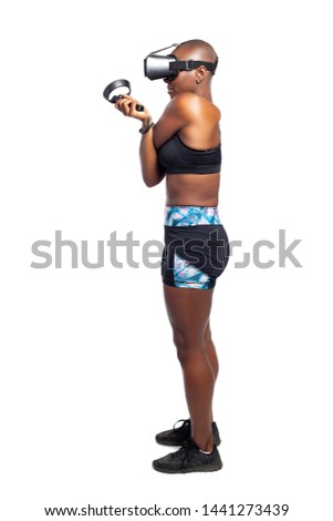 Black female wearing a virtual reality headset and holding wand controllers doing vr fitness exercises.  Gamer is in a sports simulation video game for entertainment and healthy physical activity. 