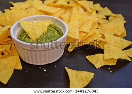 On a dark marble surface there is a heap of nachos with salt next to a bowl of homemade guacamole with onions and many spices - delicious snack with space for text