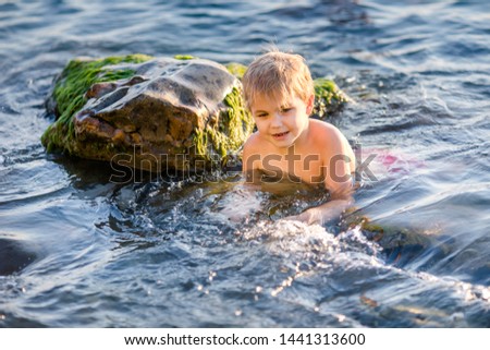 Boy splashing water during summer holidays. Attractive child having fun on a tropical beach, playing with stones and water