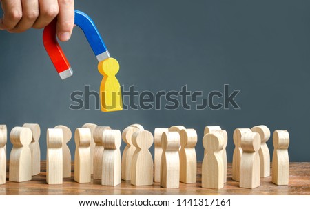A hand with a magnet pulls goldem yellow human figure out of the big crowd of people. Search for talented workers Labor migration, the demand for good specialists. Recruiting new workers, headhunters. Royalty-Free Stock Photo #1441317164