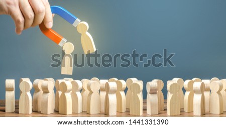 Businessman with a magnet pulls wooden figures of people out of big crowd. Recruiting workers. Formation of a new team. Search for required people and workers with the necessary talents and skills Royalty-Free Stock Photo #1441331390