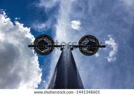Street lamp close-up on a high pole on a background of pure blue sky with white clouds