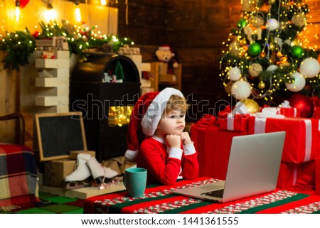 Little boy santa hat and costume. Boy child with laptop near christmas tree. Buy christmas gifts online. Christmas shopping concept. Gifts service. Santa little helper. Smart toddler surfing internet.