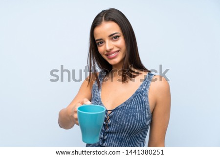 Young woman over isolated blue wall holding hot cup of coffee