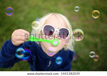 A cute little girls child is blowing bubbles while playing outside on a summer day.