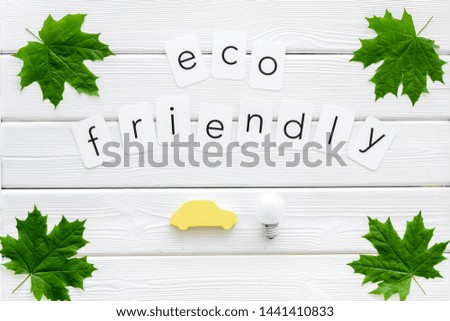 Eco friendly copy with green maple leaves, car figure and lamp for ecology concept on white wooden background top view