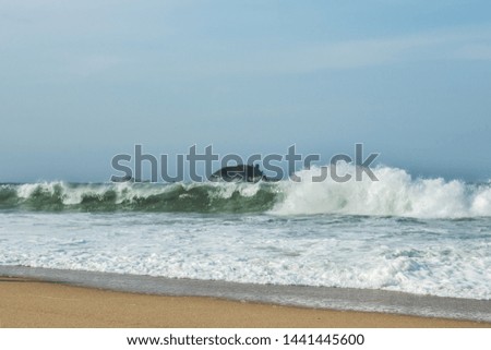 The big breaking waves during a strom at the beautiful summer sea shore background the rock island,blue sky and horizon.