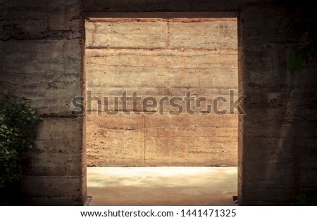 Light behind the square frame entrance. Dark background stone wall. Bare cement wall.