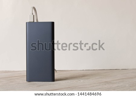 Black power Bank with adapter for charging mobile devices on a wooden table Royalty-Free Stock Photo #1441484696