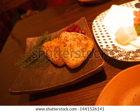 Two grilled Yaki Onigiri traditional triangle rice croquettes on decorated ceramic plate on the izakaya restaurant table