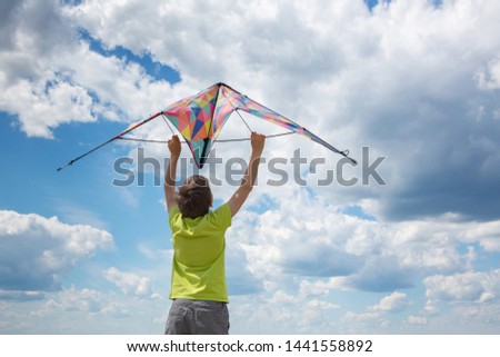 A boy with a colorful kite in his hands against the blue sky with clouds. Conceptual photography. A child in a yellow T-shirt and shorts.