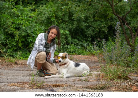 The girl in the headphones next to the dog pooch on the background of blurred green. Latino girl of appearance with dreadlocks. Communication with the animal. Fun photo. The dog