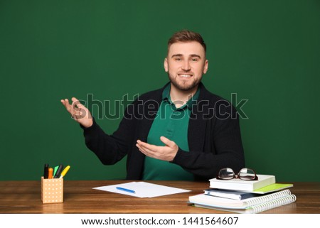 Portrait of young teacher at table against green background