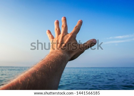 A man stretches his hand into the sea at sunset or sunrise