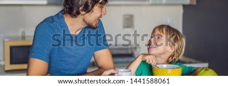 Father and son are talking and smiling while having a breakfast in kitchen BANNER, LONG FORMAT