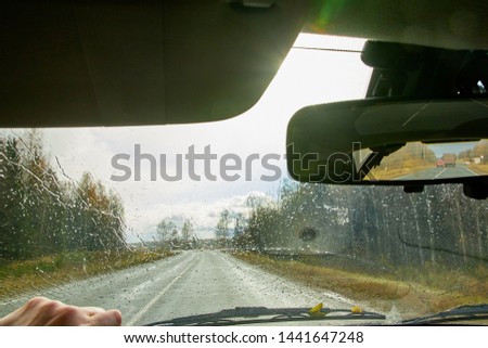 Track from the car window with drops during rain and the forest on the sidelines. Natural landscape. Woman's hand on the steering wheel