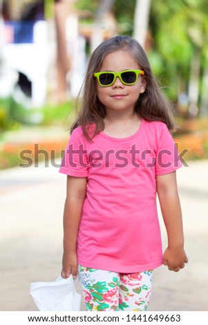 Cute little girl in fashionable sunglasses after shopping. Portrait of a kid with shopping bags. Child in sunglasses walking near shopping mall and having fun