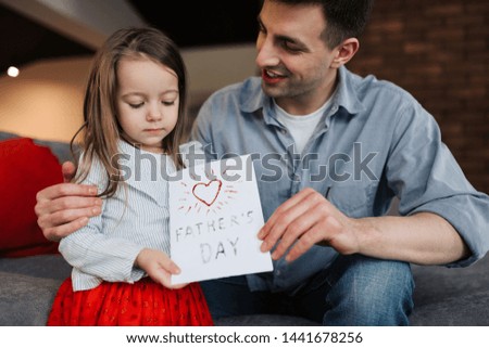 Happy father's day! Child daughter congratulates dad and gives him postcard. Daddy and girl, kissing, smiling and hugging. Family holiday and togetherness.