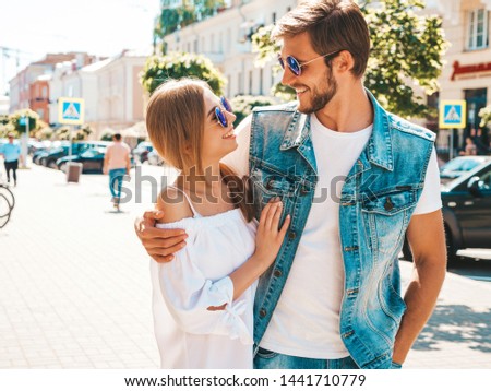 Smiling beautiful girl and her handsome boyfriend walking in the street. Woman in casual summer dress and man in jeans clothes. Happy cheerful couple family having fun in sunglasses