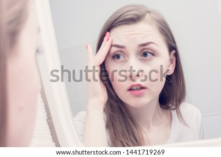Sleepy young woman, reflection in the mirror, girl is upset because of the first wrinkles looks in the mirror Royalty-Free Stock Photo #1441719269