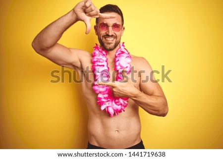 Young handsome shirtless man wearing sunglasses and pink hawaiian lei over yellow background smiling making frame with hands and fingers with happy face. Creativity and photography concept.