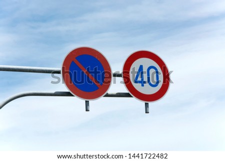 View on two round traffic signs above the road to enhance the road safety,  one sign for indication of parking regulations, the other sign to indicate speed limitation. Meant to keep road users safe.