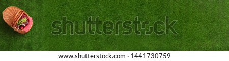 Top view of picnic basket with wine and grapes on green grass outdoor, space for text. Banner design