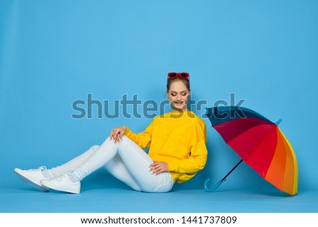      woman in a yellow sweatshirt with umbrella on a blue background                          