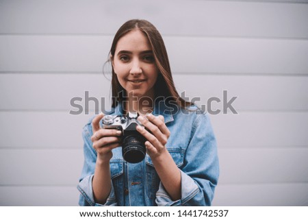 Good looking smiling hipster girl holding old fashioned equipment while looking at camera,half length portrait of positive photographer standing outdoors with vintage camera for taking pictures