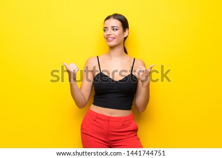 Young woman over isolated yellow background with thumbs up gesture and smiling