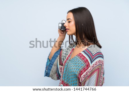 Young woman over isolated blue wall holding a camera