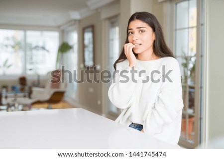 Young beautiful woman at home on white table looking stressed and nervous with hands on mouth biting nails. Anxiety problem.