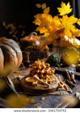 tasty homemade pumpkin orange waffles on wooden board on brown rustic table with pumpkins, spices, honey, forks, bouquet with fall leaves, yummy fall breakfast, selective focus, autumn still life