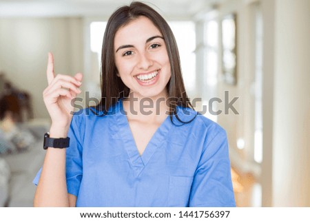 Beautiful young nurse woman at the clinic with a big smile on face, pointing with hand and finger to the side looking at the camera.