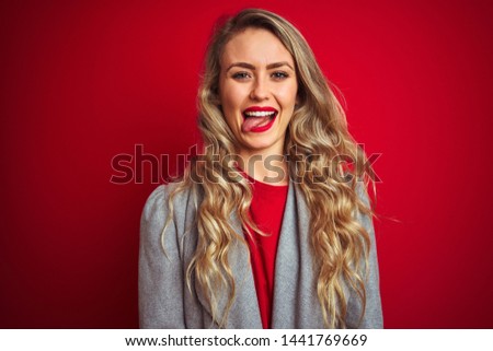 Young beautiful business woman wearing elegant jacket standing over red isolated background sticking tongue out happy with funny expression. Emotion concept.