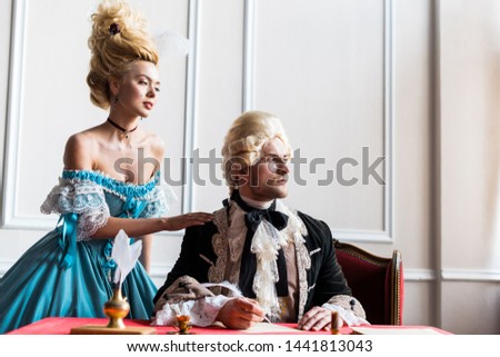 selective focus of attractive victorian woman standing near pompous man holding feather  Royalty-Free Stock Photo #1441813043