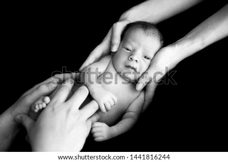 Parents hold their newborn son in their arms. Picture taken on a dark background.